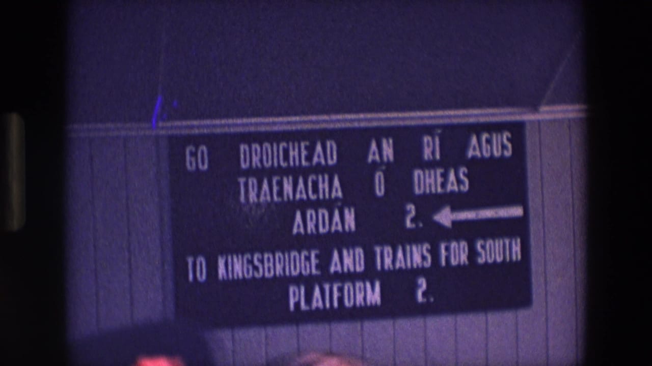1969 Ireland 8mm frame of a wall-mounted rail sign with Irish and English directions to Platform 2 for Kingsbridge and southbound trains.