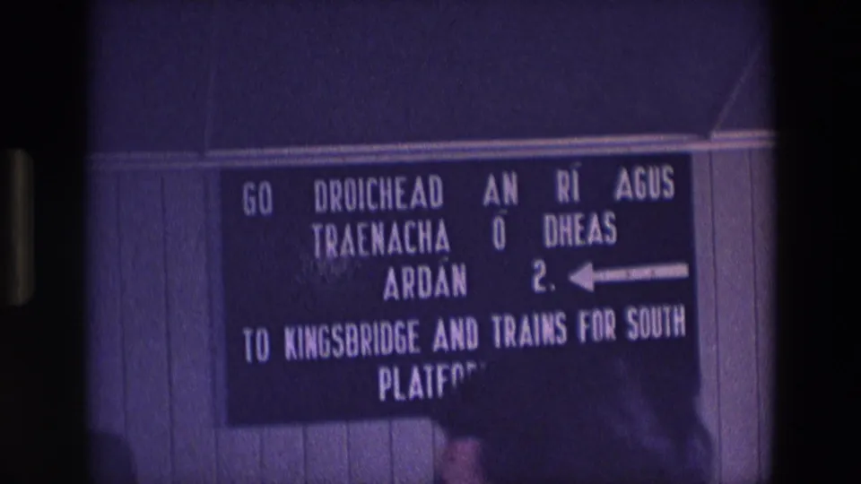 1969 Ireland 8mm frame showing the bilingual Platform 2 station sign, with the lower portion partly obscured by foreground shadow.