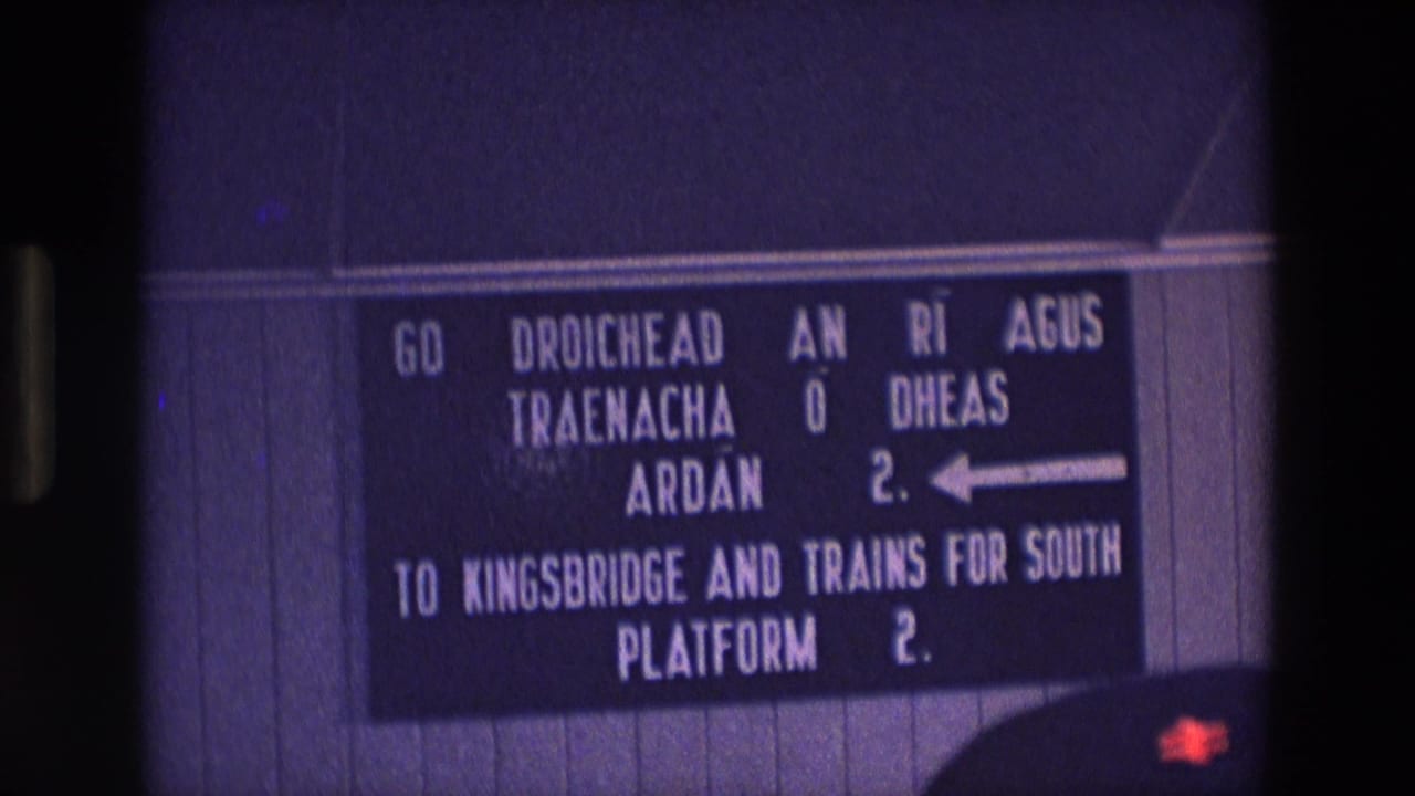 1969 Ireland 8mm frame showing a bilingual Irish and English railway station sign with a left arrow and Platform 2 directions.