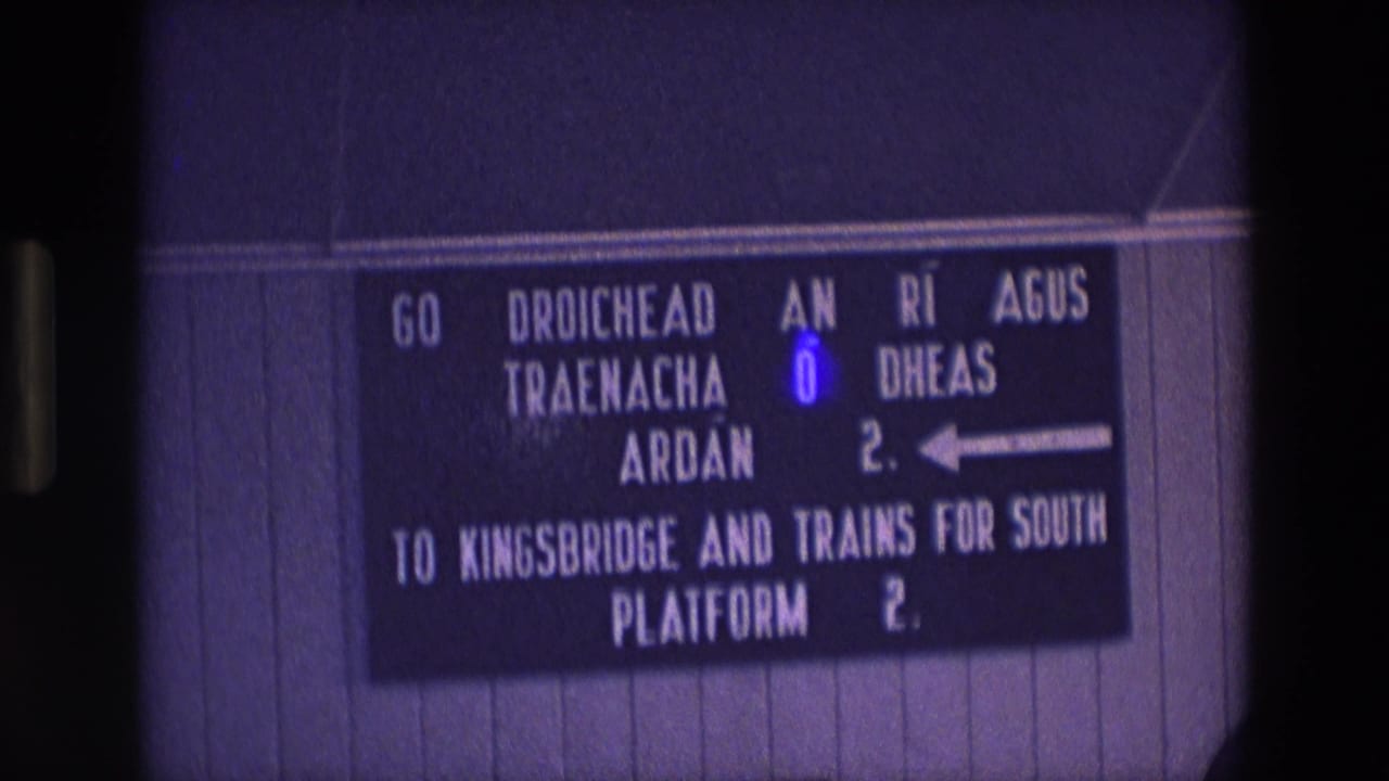 1969 Ireland railway sign in Irish and English, filmed close up on 8mm with visible grain and purple color cast.