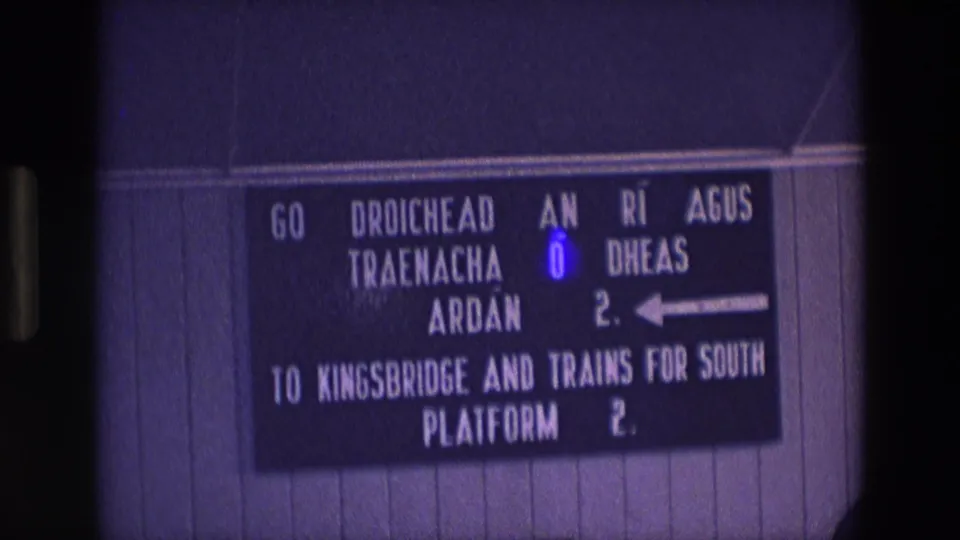 1969 Ireland railway sign in Irish and English, filmed close up on 8mm with visible grain and purple color cast.