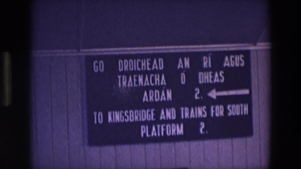 Final 1969 Ireland frame of the railway sign, with bilingual text, Platform 2 numbering, and aged 8mm film texture.