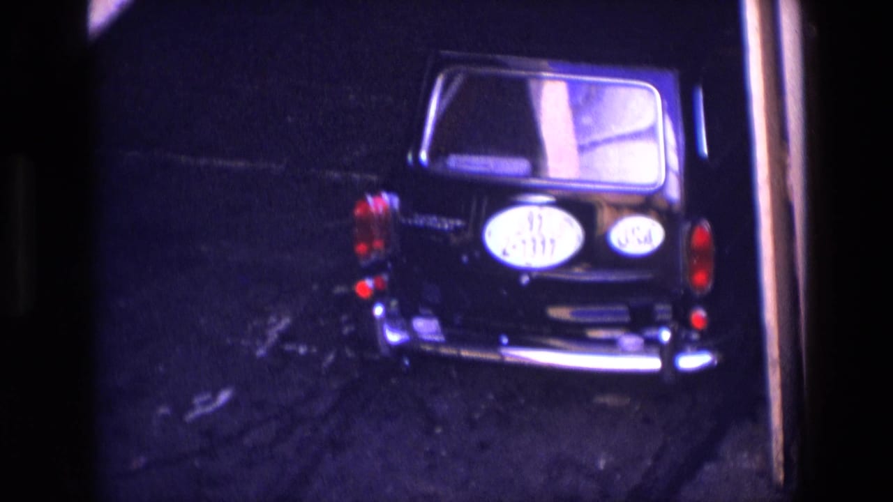 1969 Ireland home-movie frame showing a black car from behind in low light, with red taillights and an oval rear plate visible.