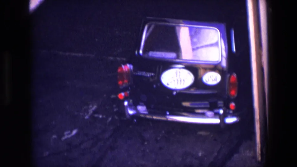 1969 Ireland home-movie frame showing a black car from behind in low light, with red taillights and an oval rear plate visible.