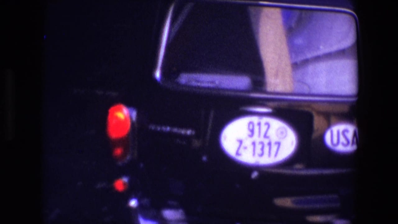 Close rear view of a black car with oval plate, USA sticker, and red taillight.
