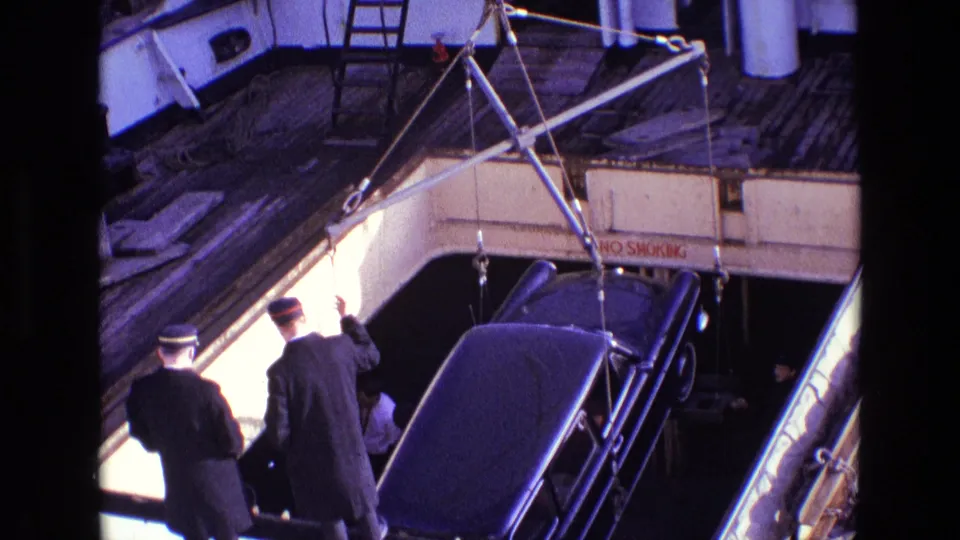 1969 Ireland shipboard view of a black car suspended or lowered by a crane, with uniformed men supervising on deck.