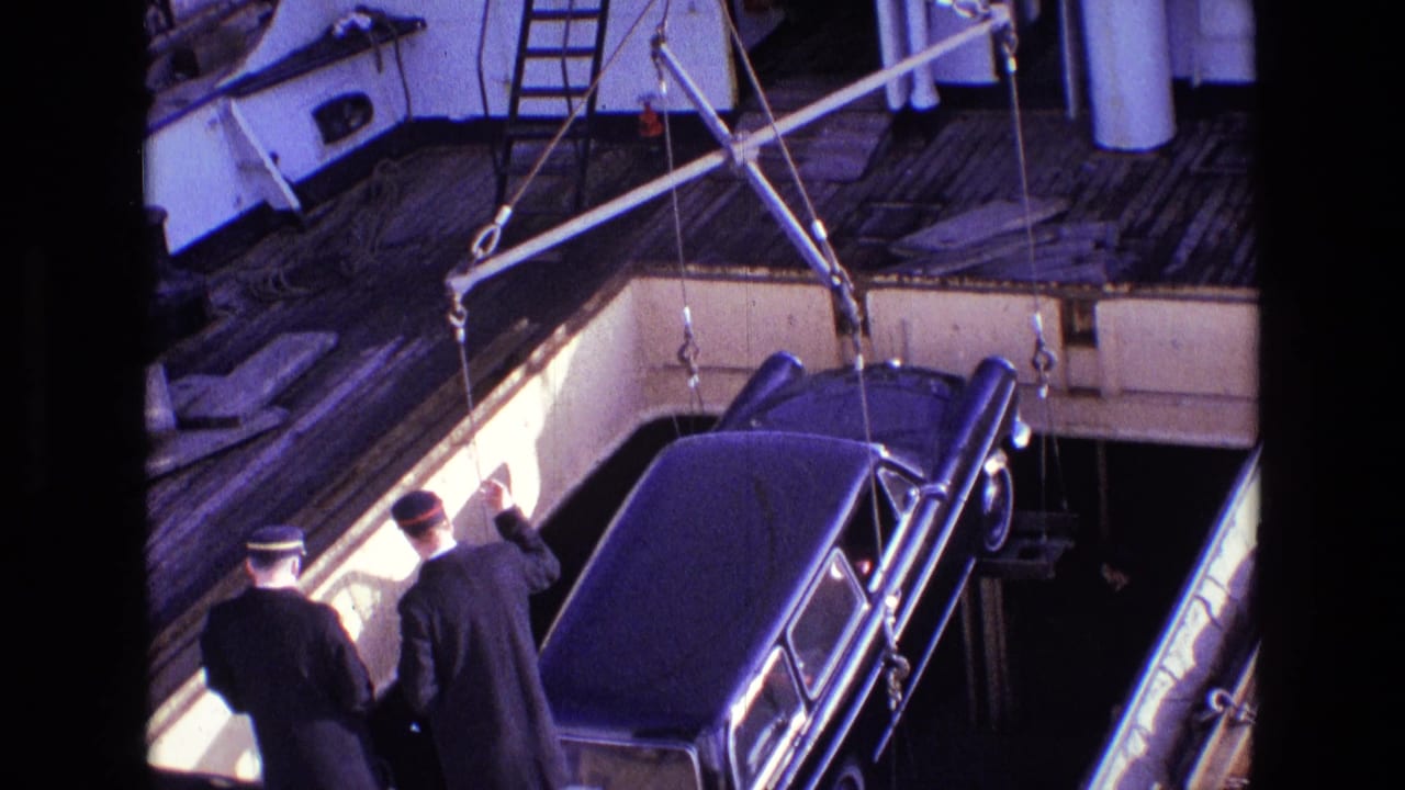1969 Ireland 8mm frame showing crew in dark uniforms supervising a black vehicle suspended over a ship deck.