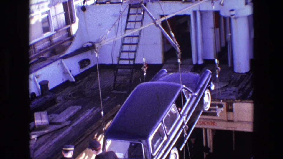 The black vehicle is suspended above the deck as ship fittings, ladders, and rigging fill the background.