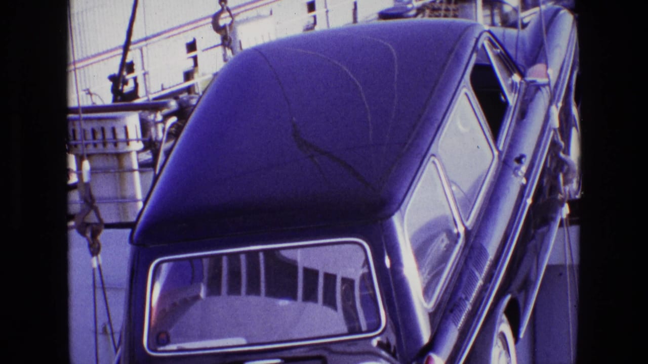 Rear of a dark station wagon hanging at an angle beside ship railings.