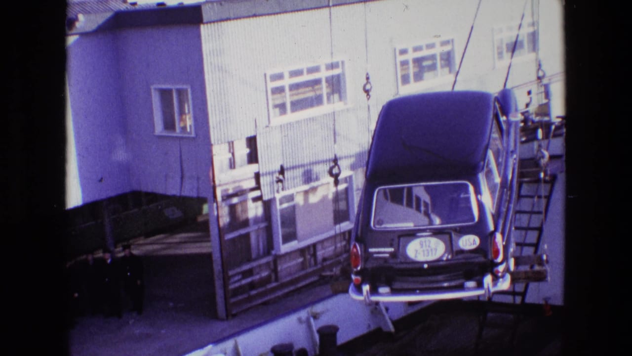 1969 Ireland dockside view of a black hearse hanging from hoist cables near a corrugated building as men watch from below.