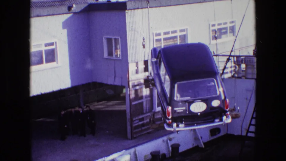 The hearse appears to move lower or farther across the dockside rigging area, with the building, ladder, and observers still visible.