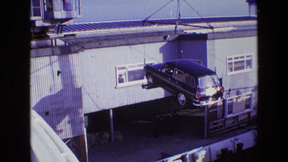 The black hearse is carried by crane near the building facade, with a man still visible at the window and worksite shadows below.