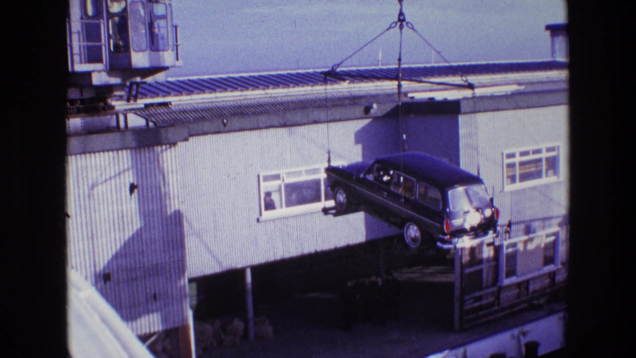 1969 Ireland 8mm frame showing a dark estate car hanging from crane cables near dockside windows and corrugated siding.