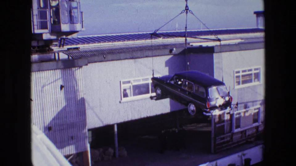 1969 Ireland 8mm frame showing a dark estate car hanging from crane cables near dockside windows and corrugated siding.
