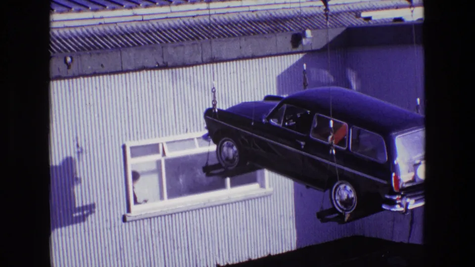 A closer 8mm view shows the estate car lifted past building windows, with rigging attached at the front and rear.