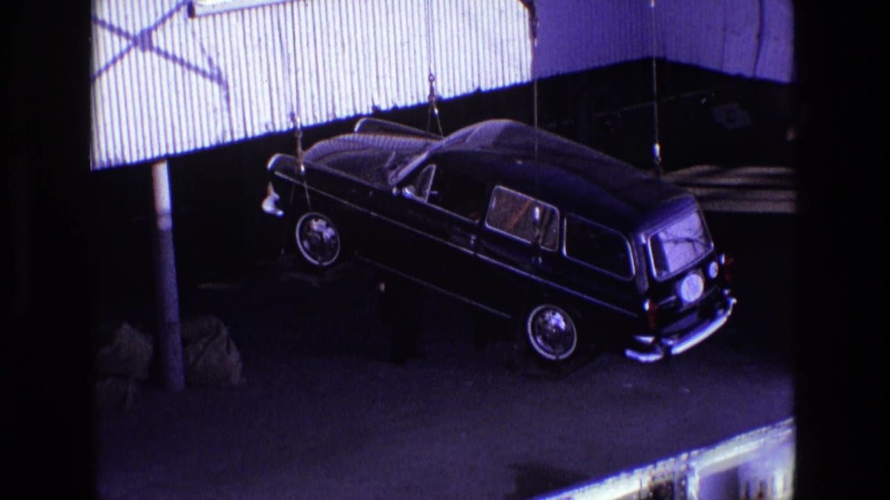 Suspended black station wagon angled near a dock building and shadowed pavement.
