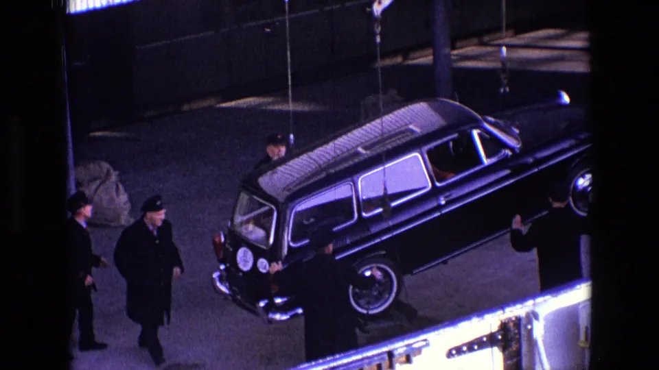 The 1969 Ireland footage shows the hearse closer to camera, suspended beside men in dark coats at the dock.