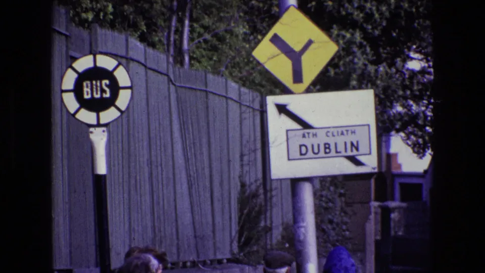 1969 Dublin street-sign view with BUS stop marker, Y-intersection warning sign, ATH CLIATH DUBLIN sign, and a partly visible person near the lower edge.