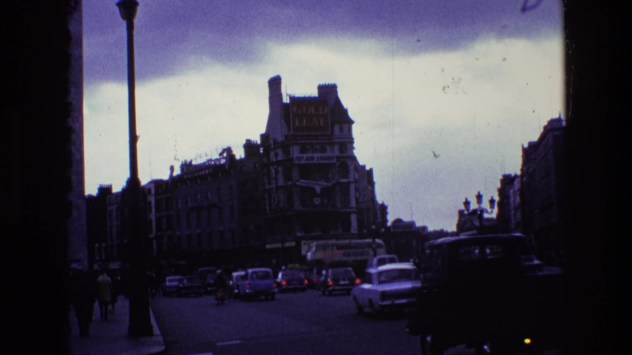 Vintage cars and pedestrians on a broad street beside buildings with visible advertising signs.