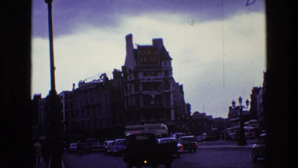 Late 1960s Irish street scene with traffic, pedestrians, dark foreground framing, and period commercial signs.