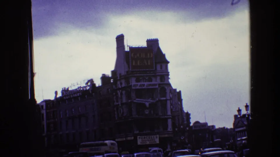 1969 Ireland street view with older buildings, a large Gold Leaf sign, traffic below, and dark window-frame edges.