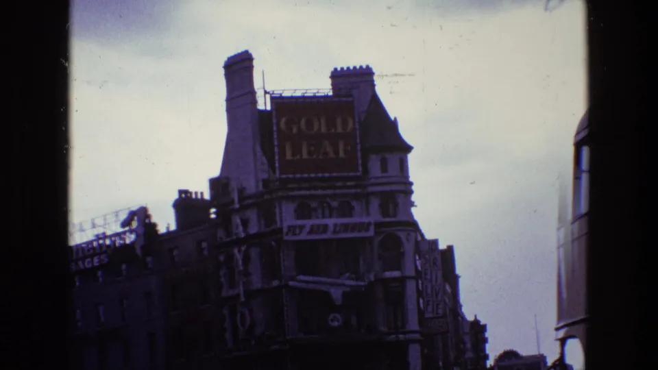 1969 Ireland street view with a large Gold Leaf sign, older commercial buildings, traffic, and the edge of a vehicle or bus at right.