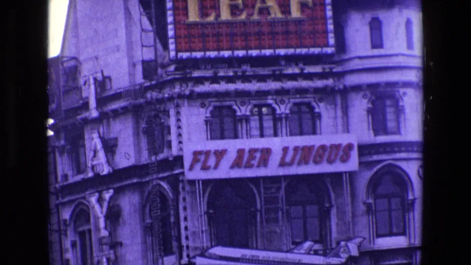 1969 Ireland close-up of an ornate facade carrying a Fly Aer Lingus banner, with the lower edge of a Gold Leaf billboard above.