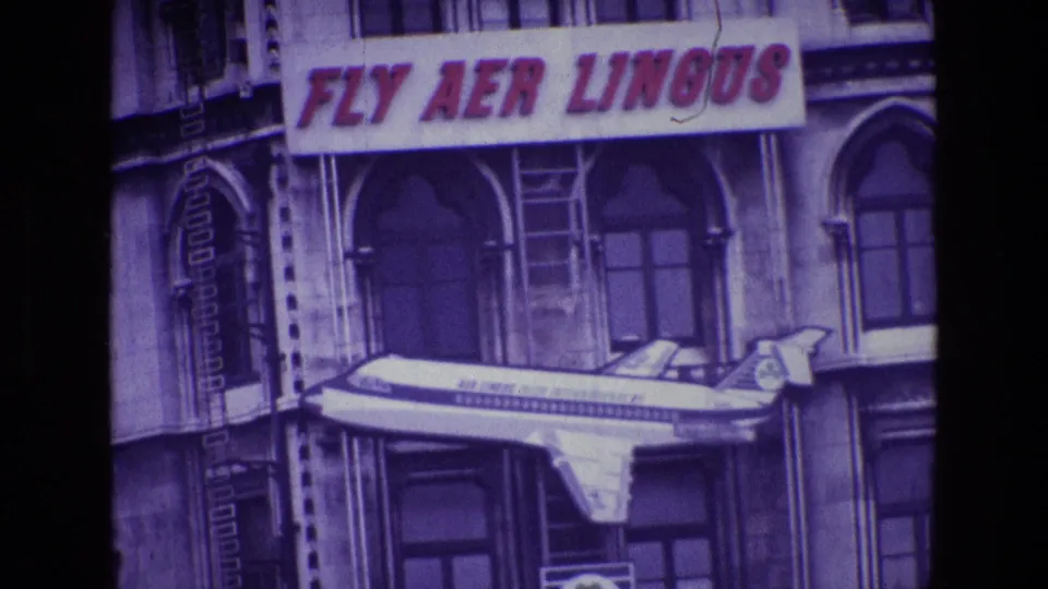 1969 Ireland frame with the camera tighter on the FLY AER LINGUS banner, arched windows, and mounted aircraft model.