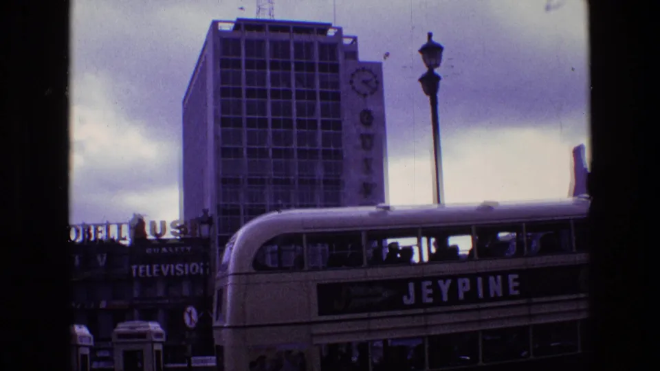 A Jeypine double-decker bus turns through a London street scene with Guinness signage, television sign text, and period street traffic.