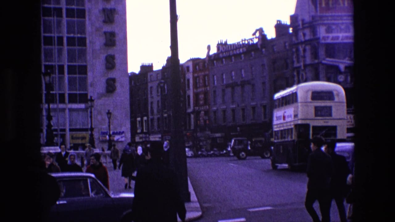City street with pedestrians, shopfronts, cars, and a double-decker bus in the distance.