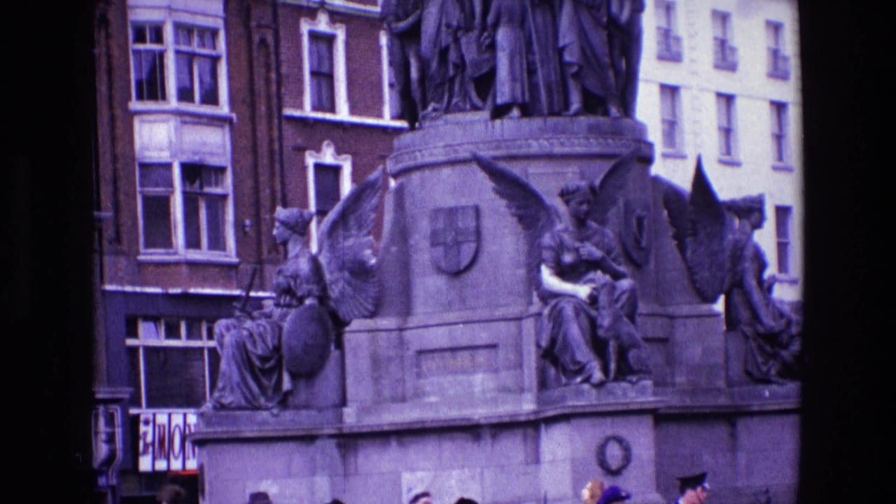 1969 Ireland 8mm frame showing a stone civic monument with winged figures, nearby buildings, and partial pedestrians below.
