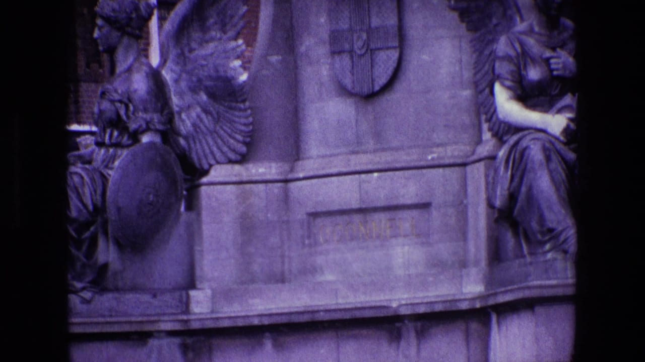 Close view of monument base with winged figure, shield emblem, seated sculpture, and engraved stone.