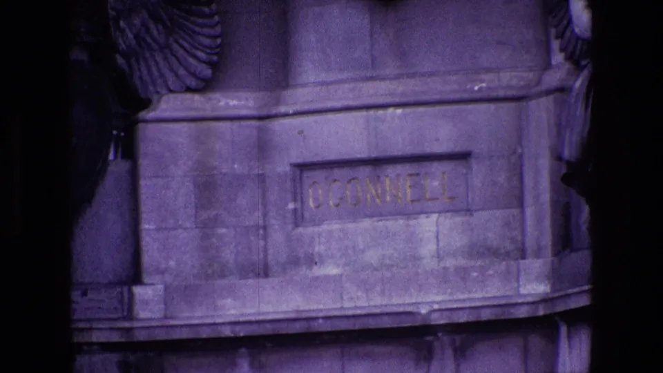8mm frame focused on the monument base where O'Connell is engraved into stone beneath a large sculpted wing.