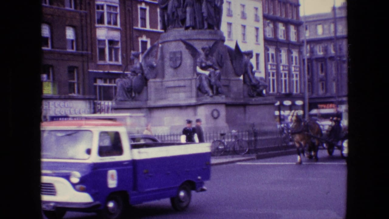 1969 Ireland street view with a blue-and-white van, pedestrians, a horse carriage, and a large stone monument in the background.