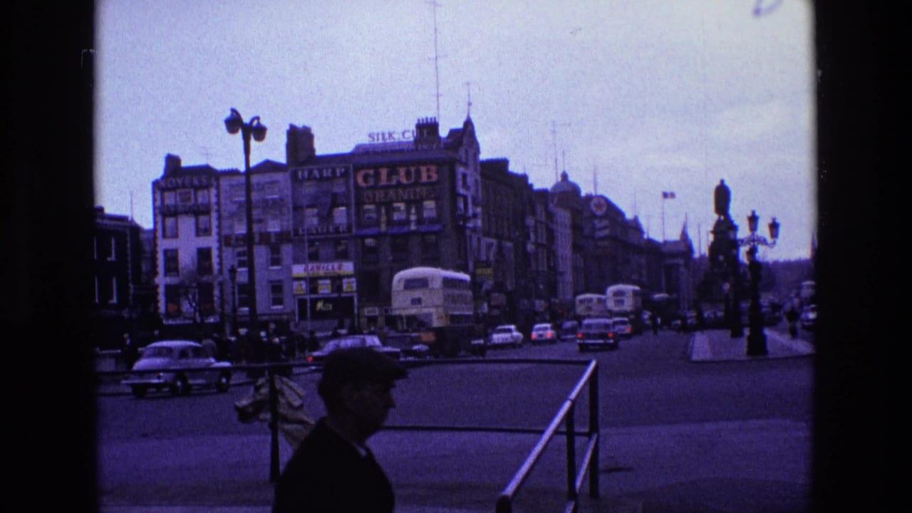 Intersection with buses, cars, a pedestrian silhouette, railings, streetlamps, and large building signs.