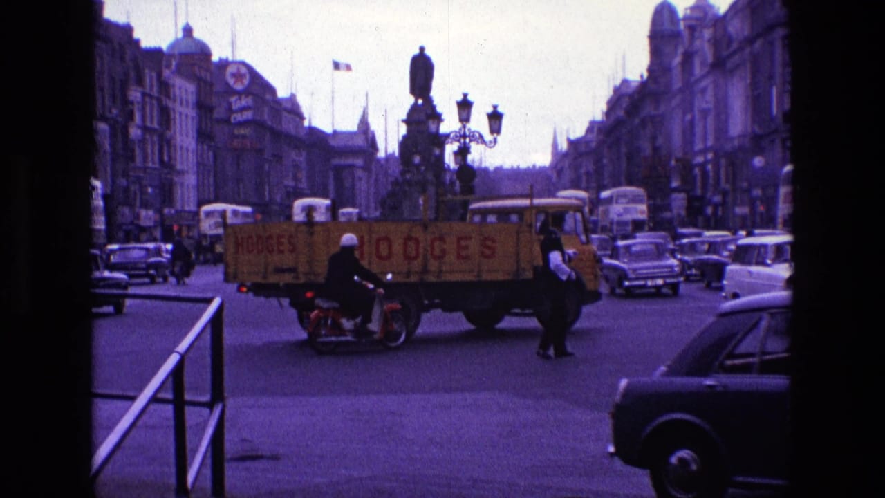 1969 Ireland intersection with a yellow HODGES truck, classic cars, a bus, pedestrians, a motorcyclist, and a uniformed officer visible.