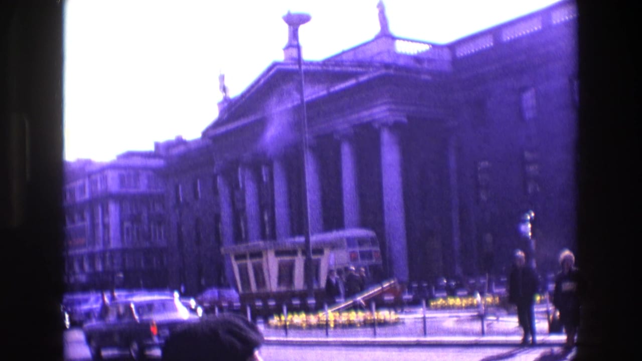 1969 Ireland street view with a double-decker bus, period cars, pedestrians, and a large columned building.