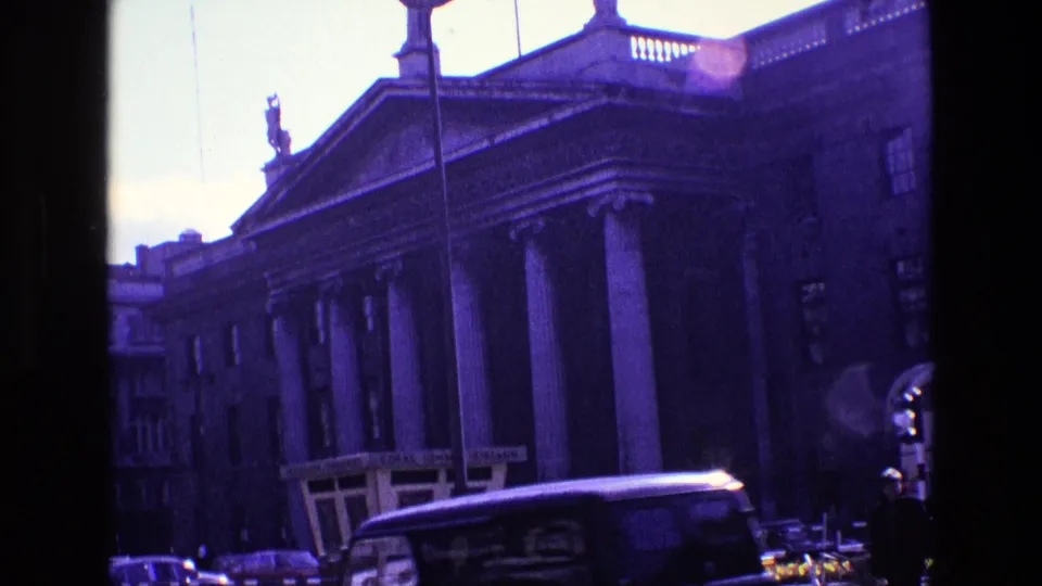 A dark vehicle or bus moves across the foreground of the 1969 Ireland street view, with columns behind it.