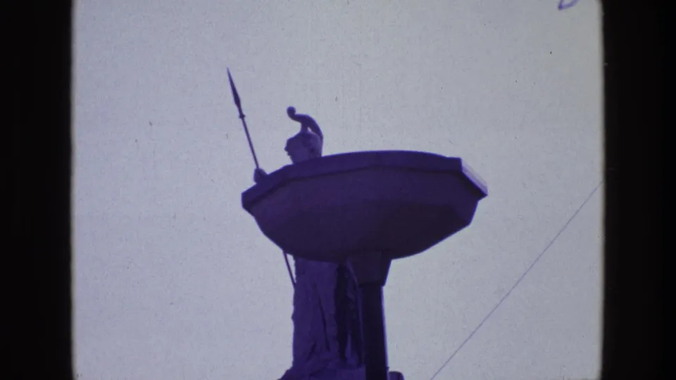 Closer 8mm view of the Irish rooftop guardian statue, with the spear and tall pedestal silhouetted in blue-purple tones.