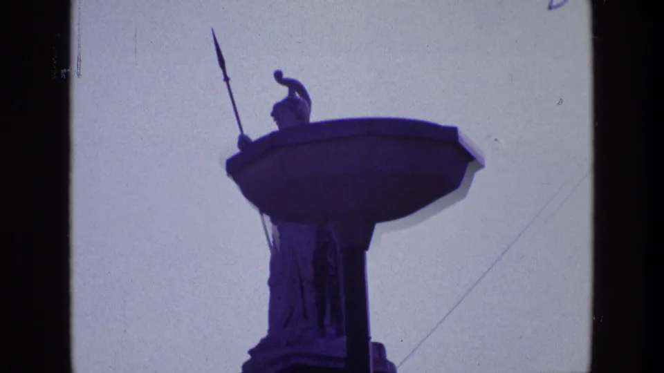 Close 1969 Ireland frame of the spear-holding guardian figure on a high pedestal, with roof detail cropped at the lower edge.