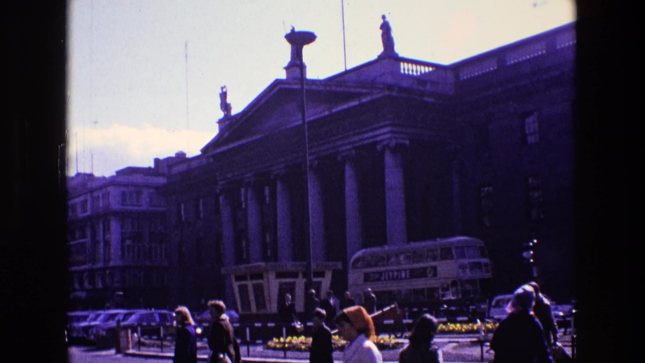 1969 Ireland street view with pedestrians, vintage cars, a bus, and a large neoclassical building with columns and roof statues.