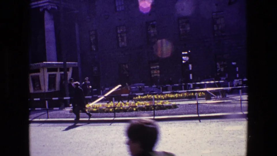 1969 Ireland city street view with pedestrians, railings, bright sun, parked or moving cars, and a large neoclassical facade.