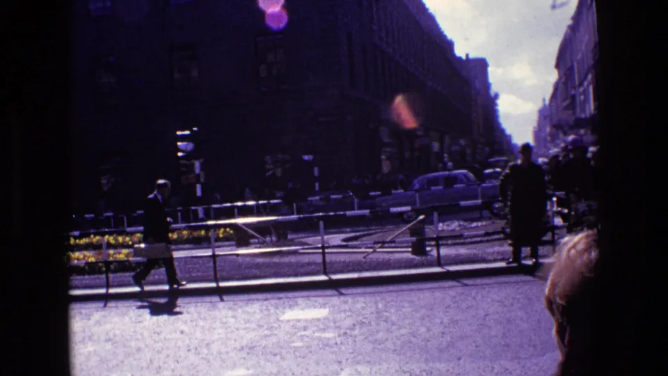 Urban Ireland street scene from 1969 with pedestrians, classic cars, railings, masonry buildings, and strong purple film cast.