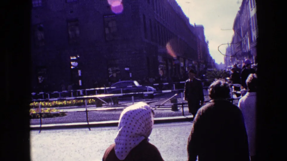 Late 1960s Ireland street view with pedestrians in the foreground, a white headscarf, older cars, railings, and tall urban buildings.