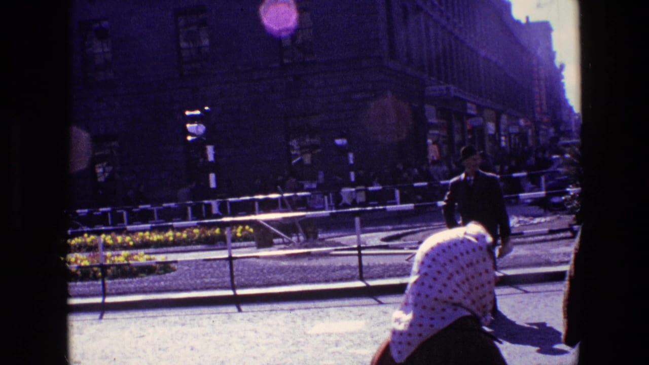 1969 Ireland street view with a yellow flower median, metal railings, pedestrians, older cars, and a woman in a white polka-dot headscarf.