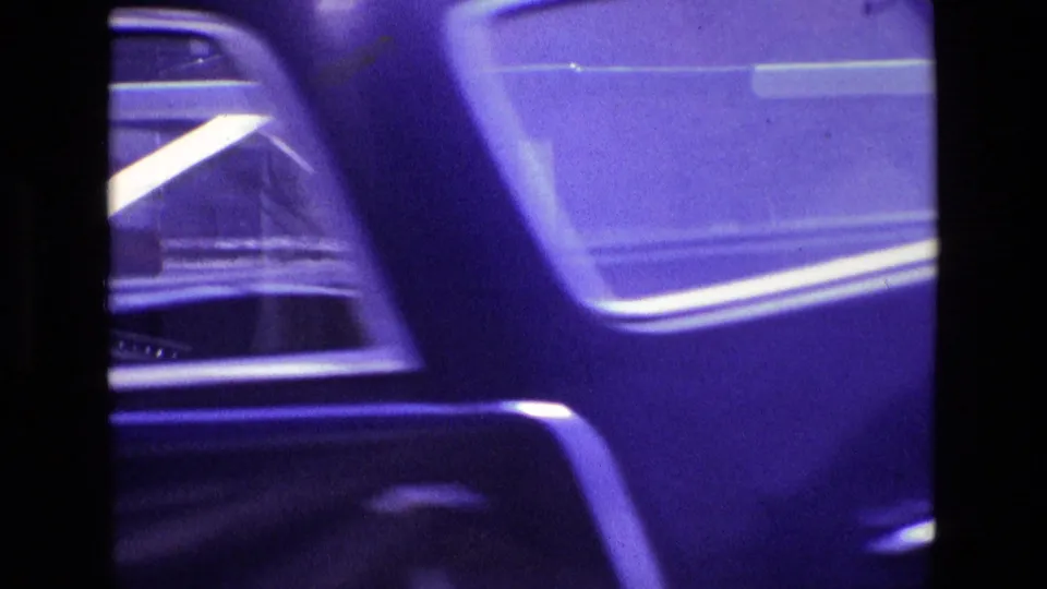 A blue-toned car passes close to the camera, partly obscuring the flower bed and barrier in this 1969 Ireland street view.