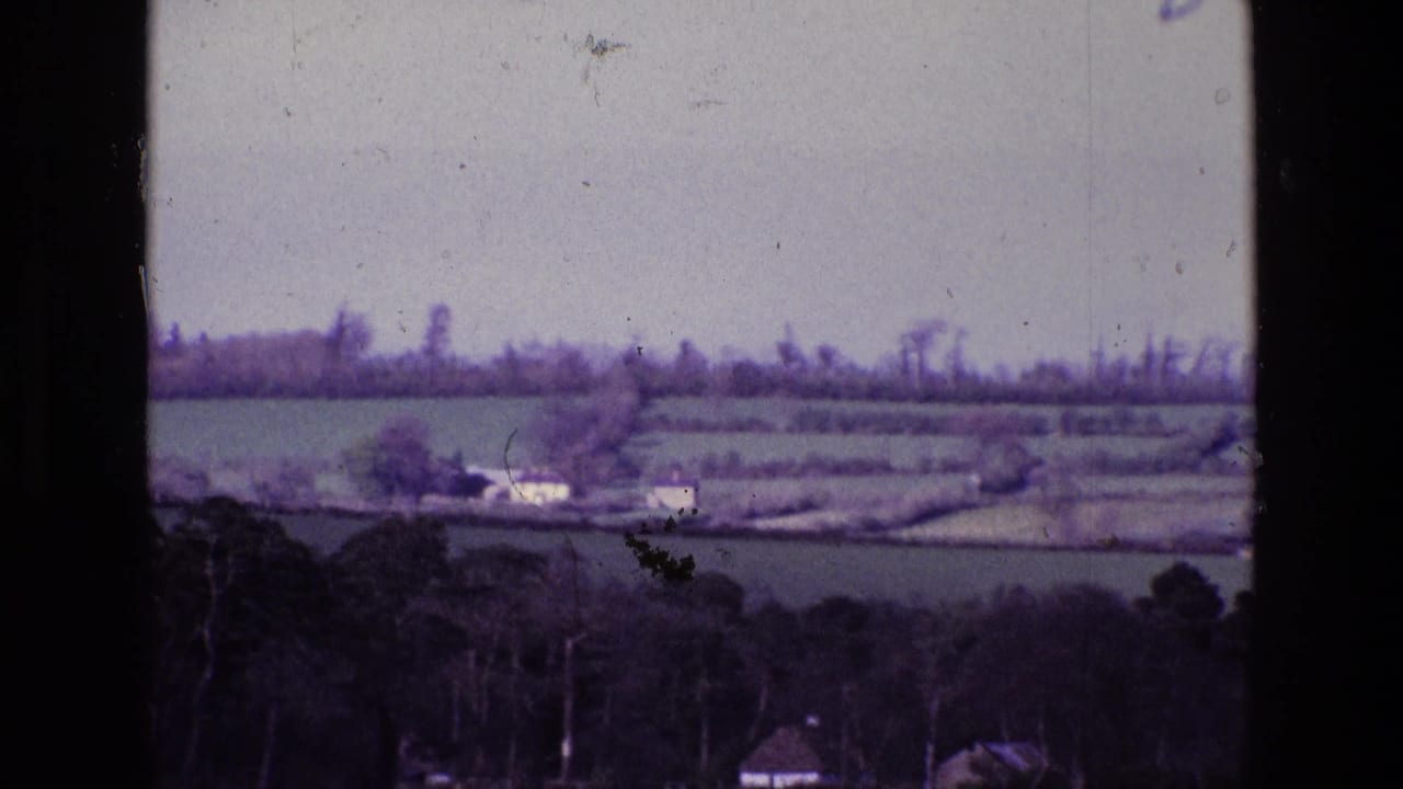 Distant farm buildings and fields beyond a dark wooded foreground.