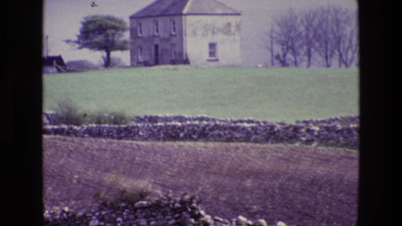 Stone-walled fields below a plain building on a grassy hill.