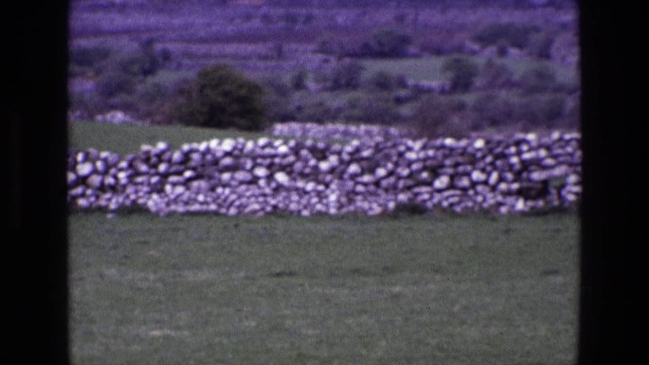 Dry-stone wall across a grassy field with distant hills and dark film borders.