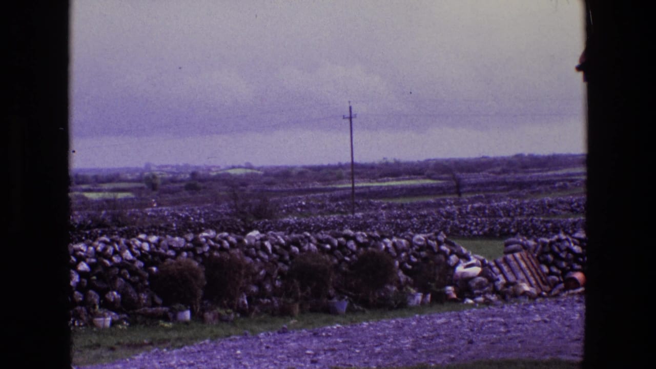 Stone walls and fields seen past a building edge, with a utility pole and cloudy sky in the distance.